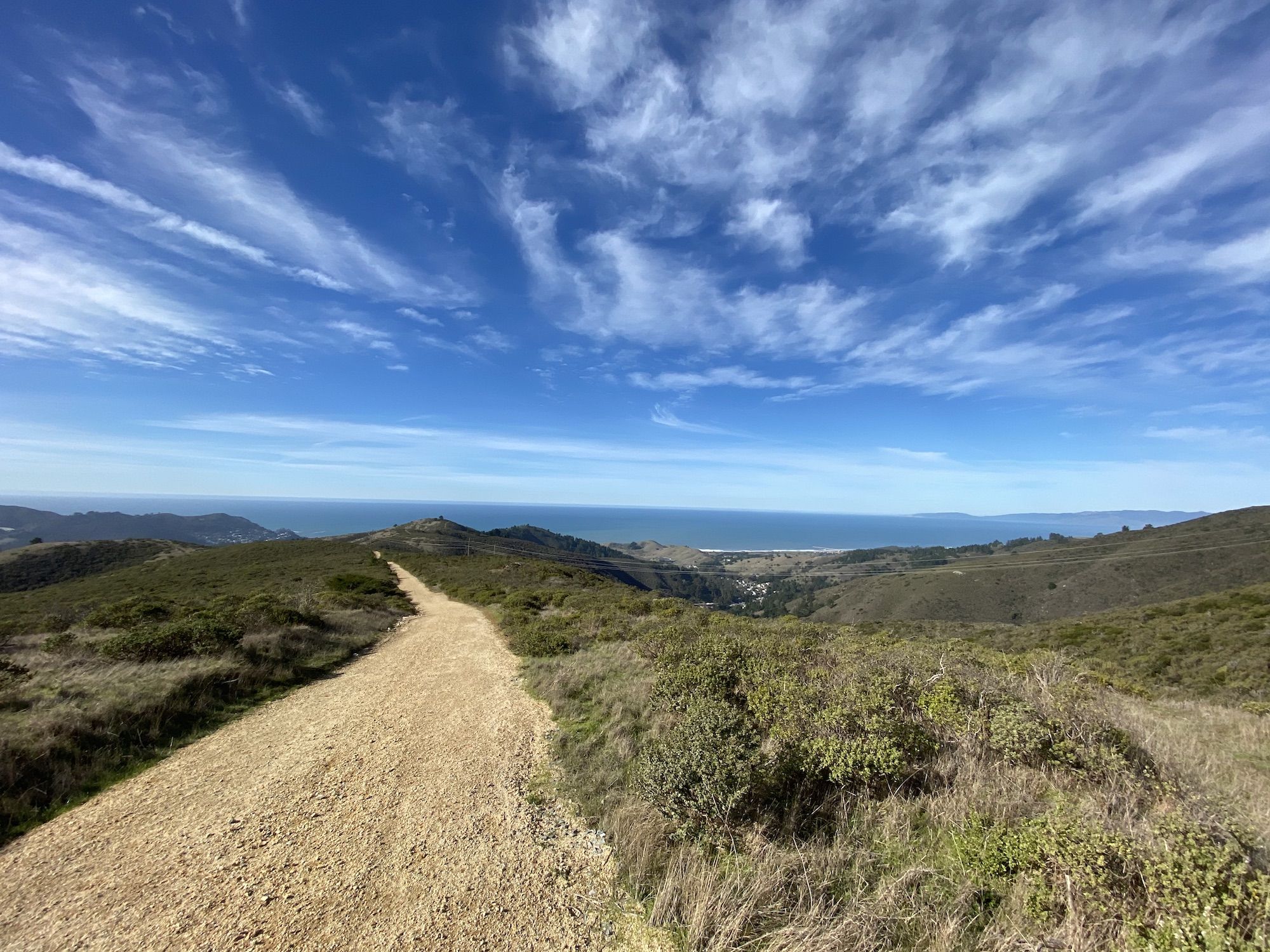 A dirt road over mountains leading towards the ocean