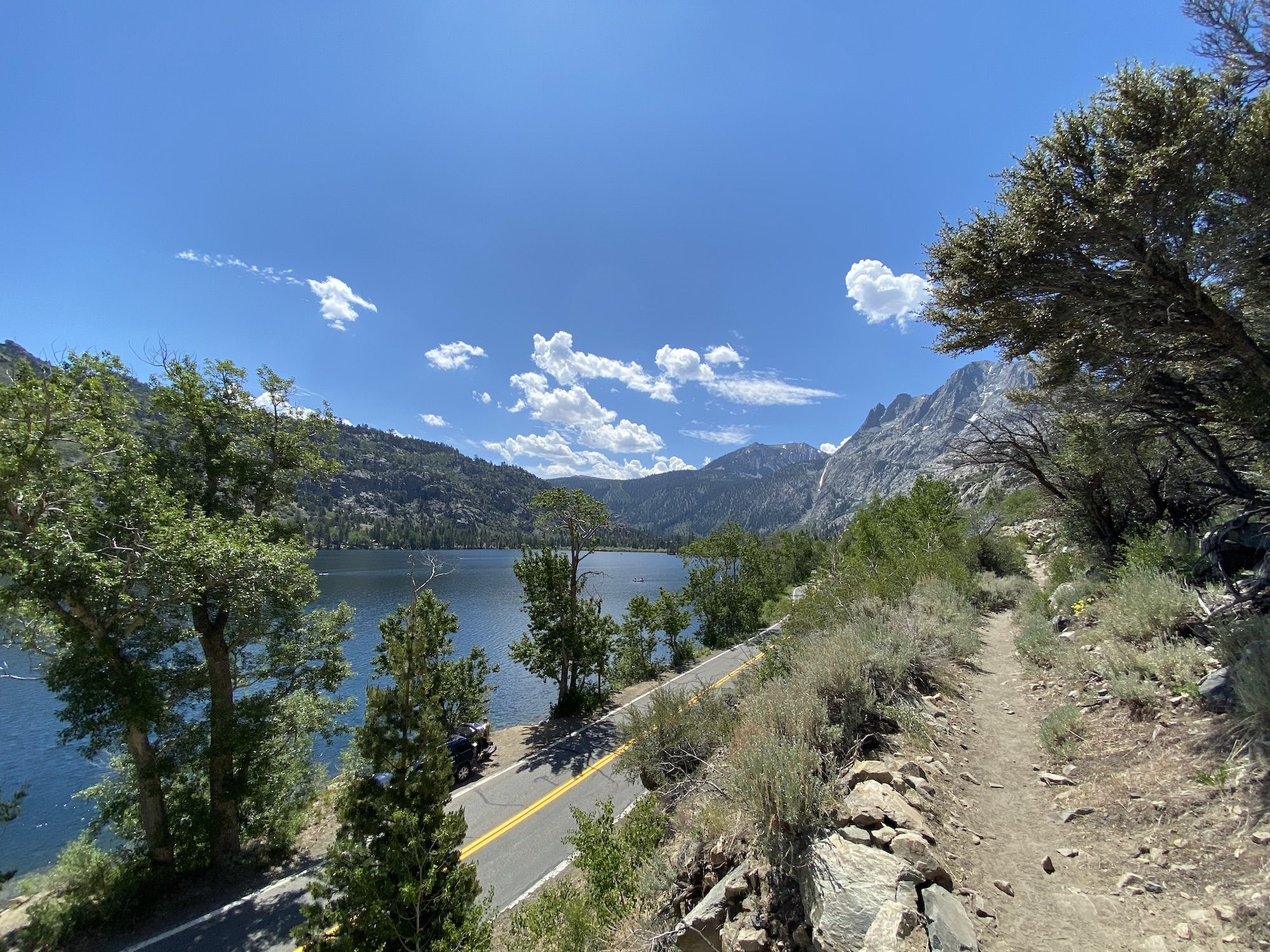 A dirt trail following a road next to a lake.