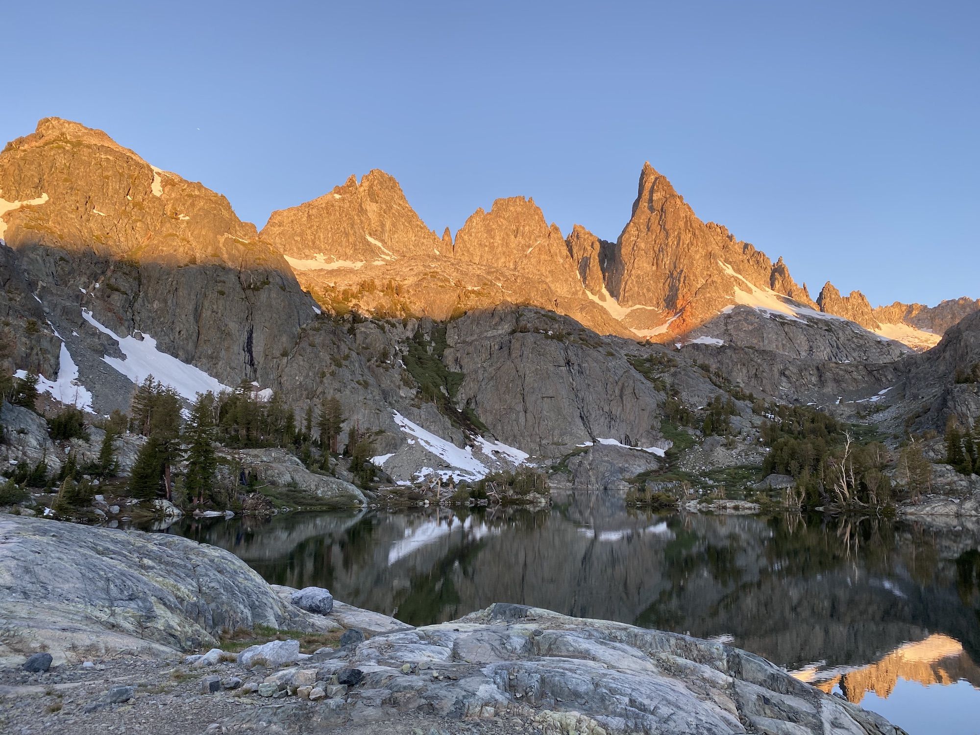 The sun is lighting up the upper half of the mountains surrounding a lake