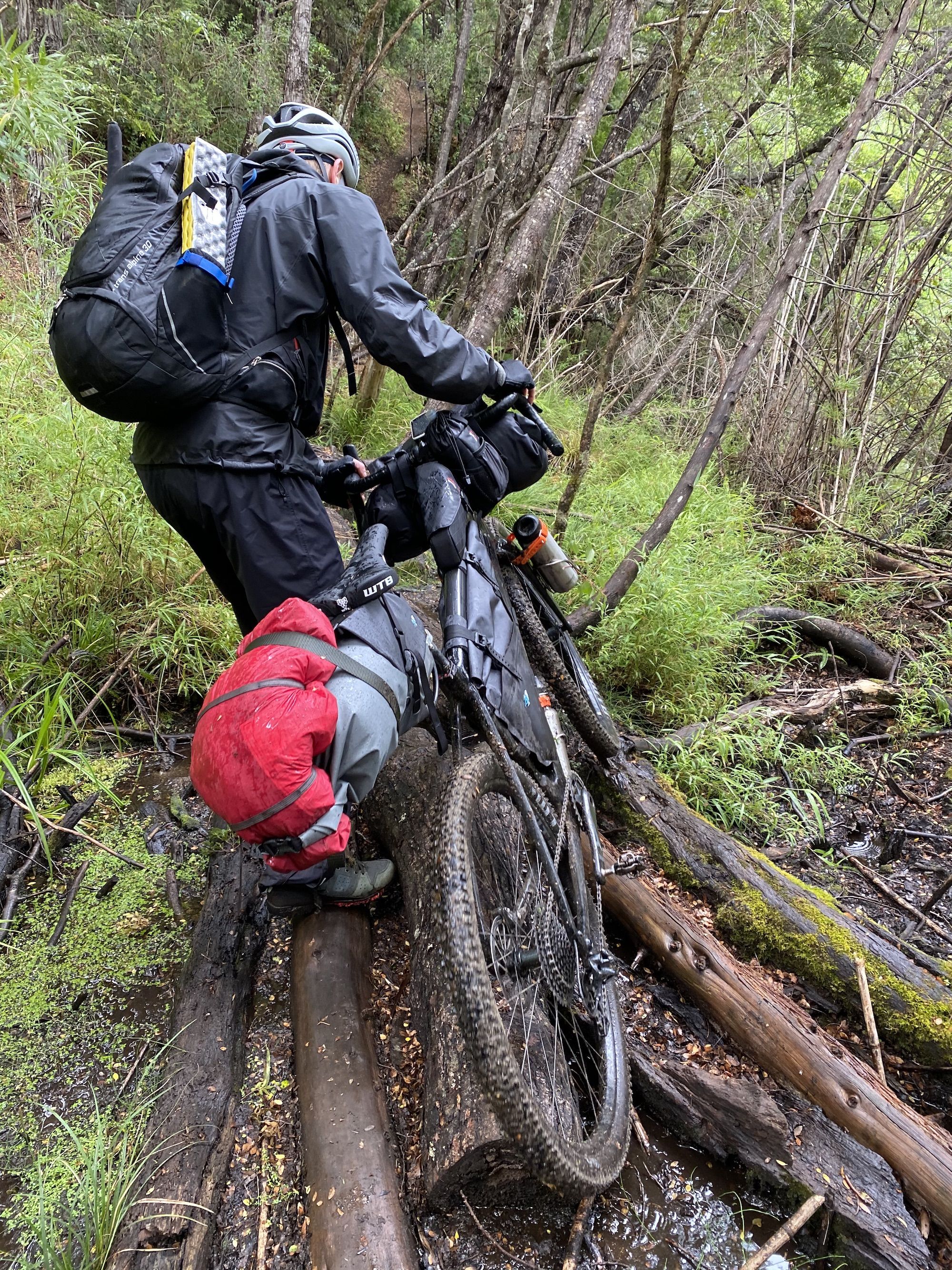 A man dragging a bike over wet logs
