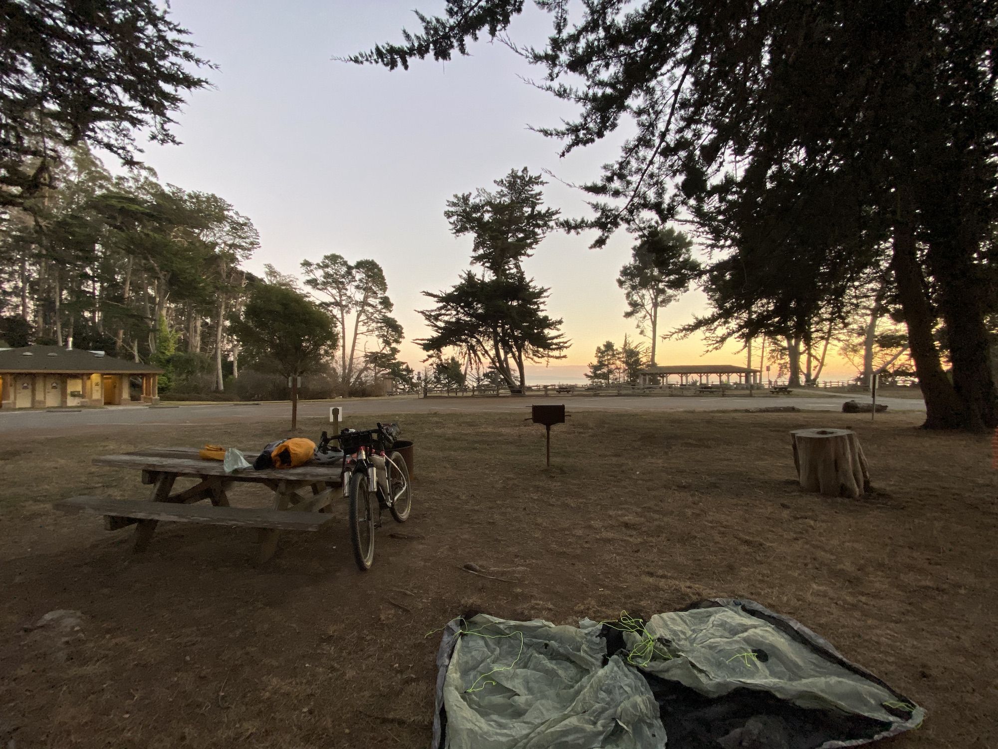A gravel bike leaning against a table with a tent in the foreground and the Pacific Ocean in the background. 