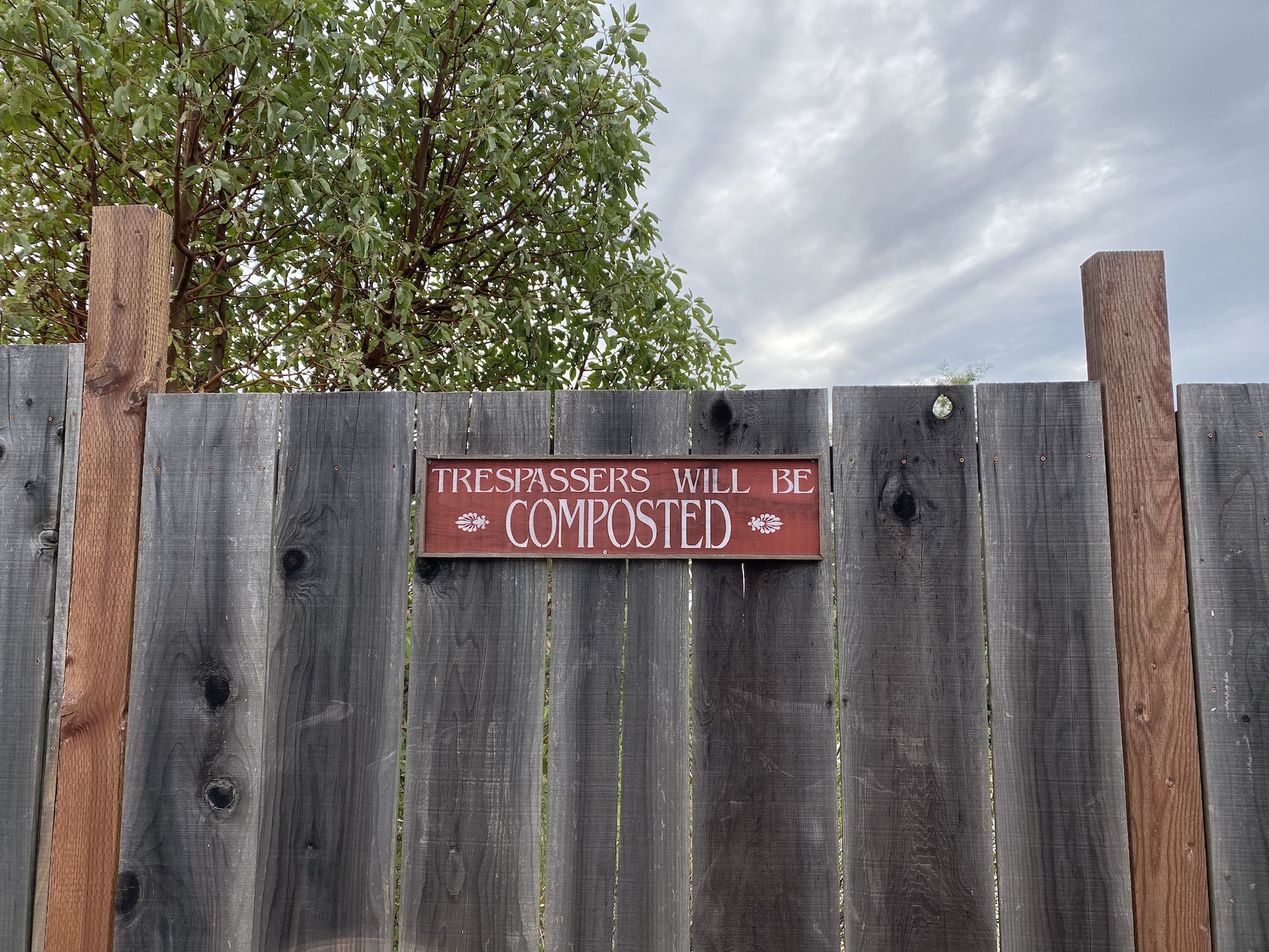 A fence with a "Trespassers will be composted" sign. 