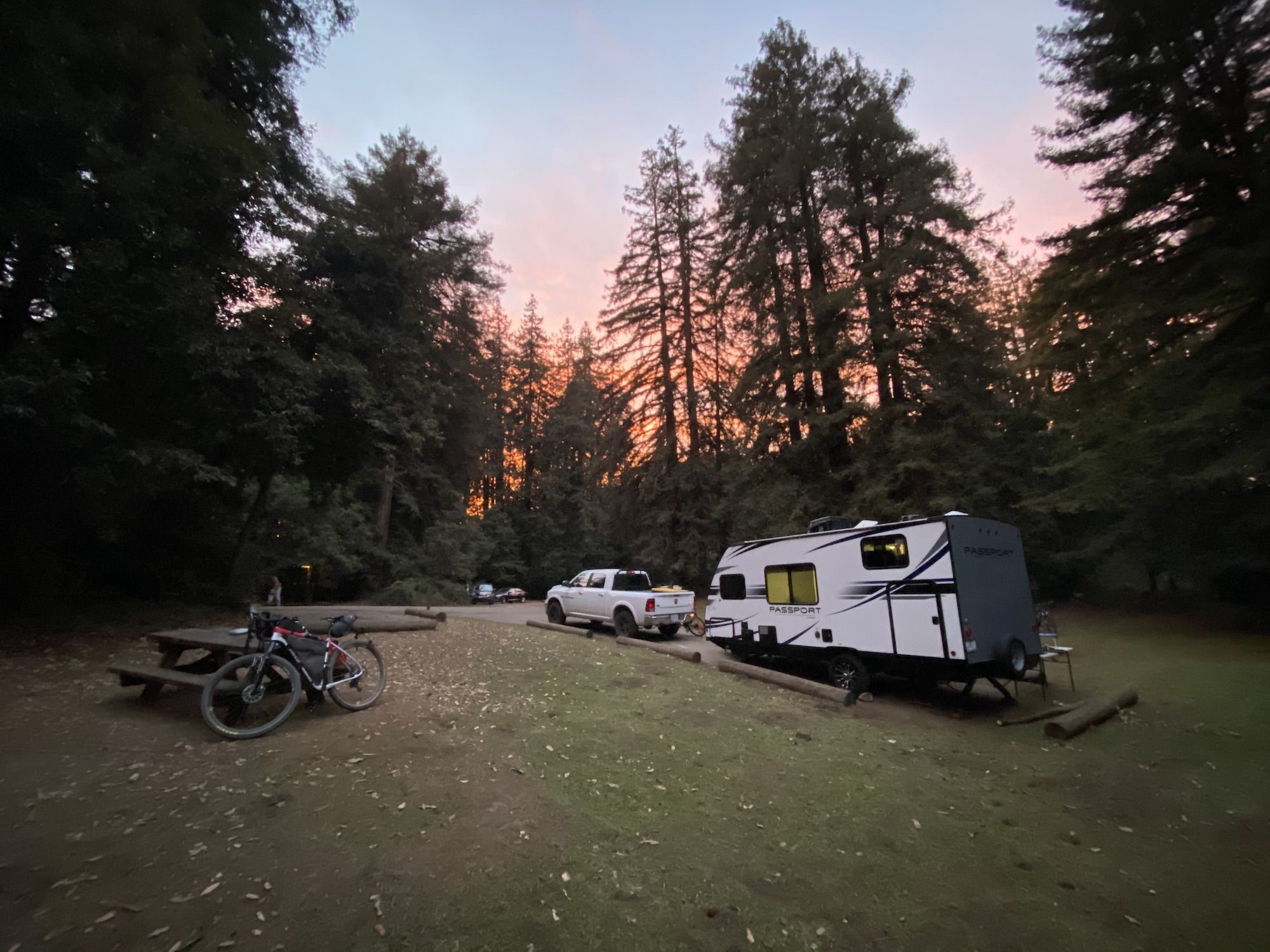 On the left: a bike leaning against a table. On the right: a pickup and a camper. 