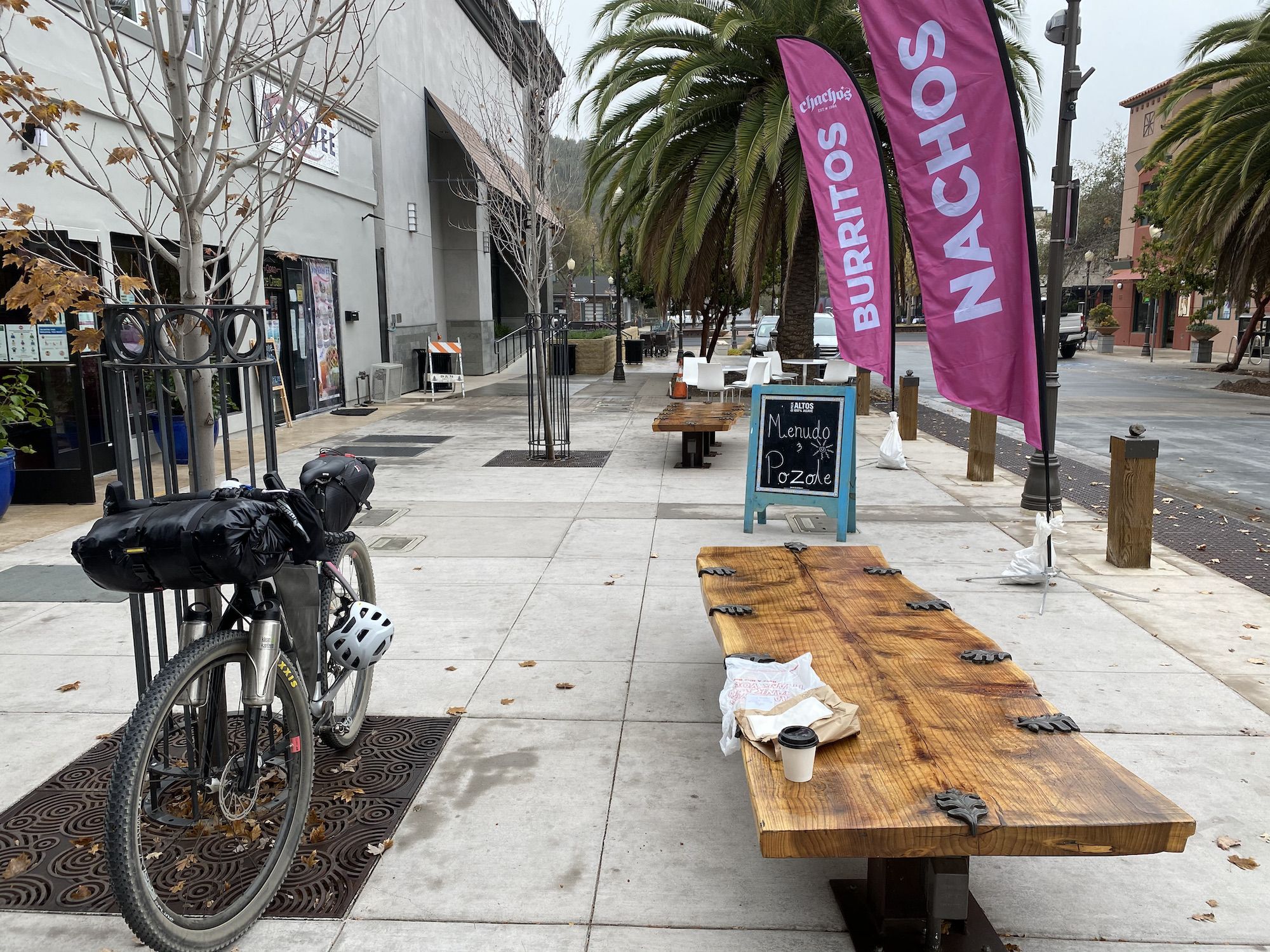 A bike leaning against a tree next to a bench outside a Mexican restaurant. 