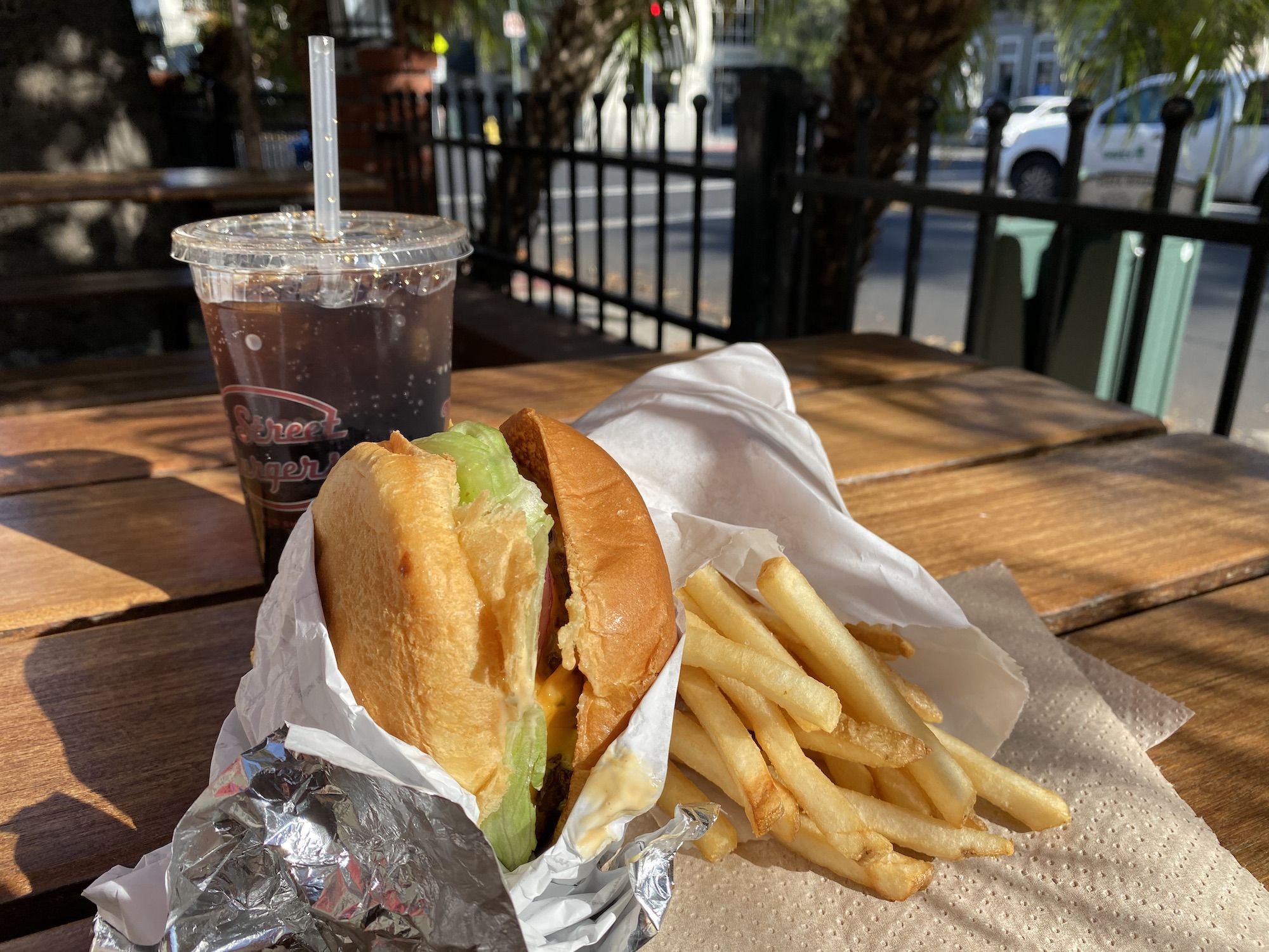 A double cheeseburger, fries, and drink on a table outside.