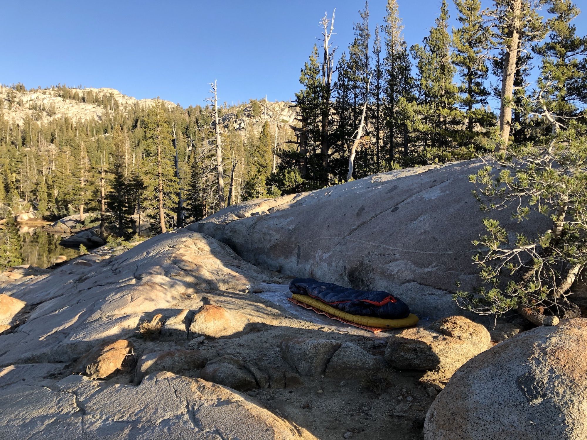 A sleeping bag on a pad laying on a small flat spot on a big cliff.