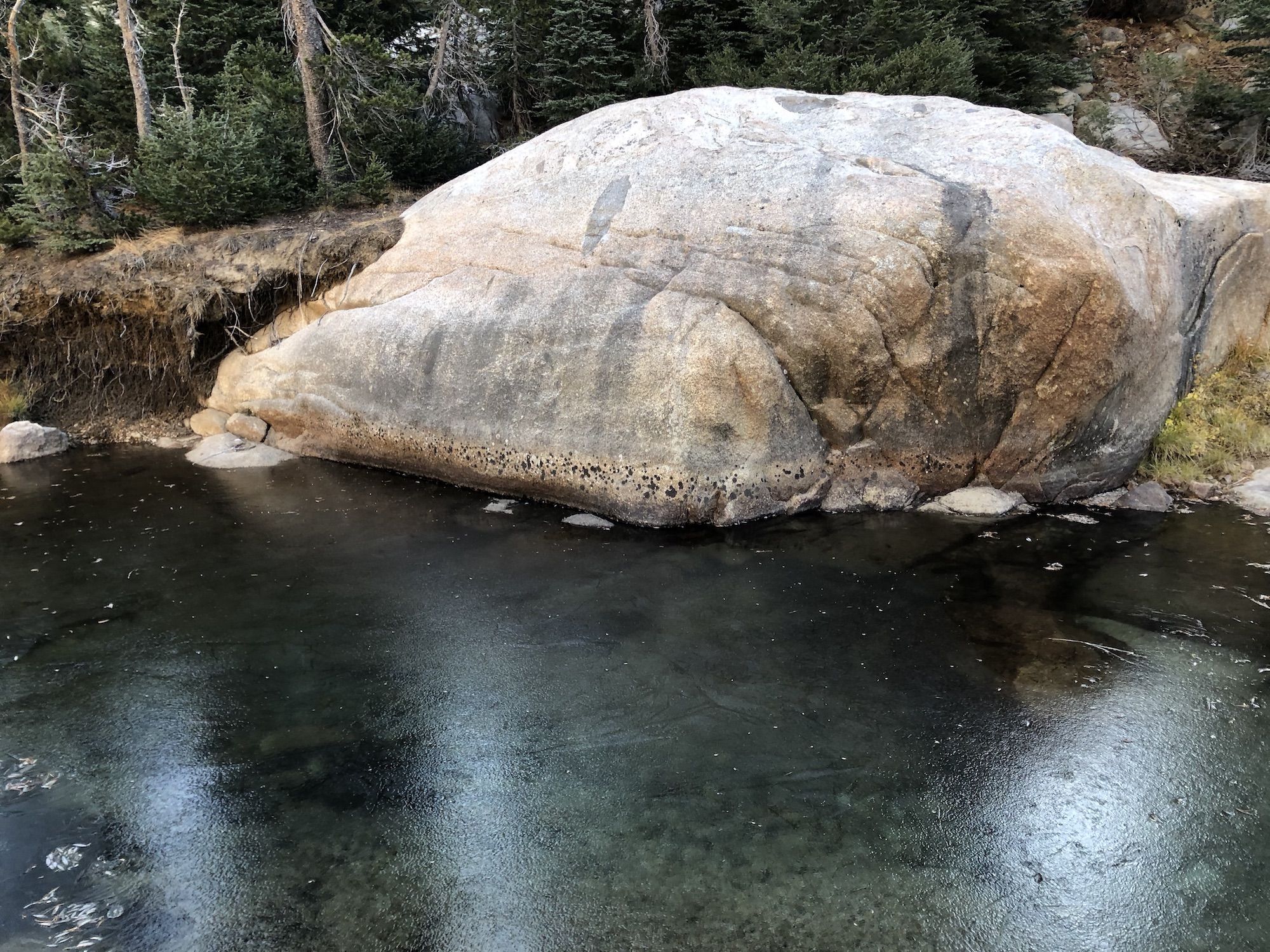 A frozen creek next to a large boulder.