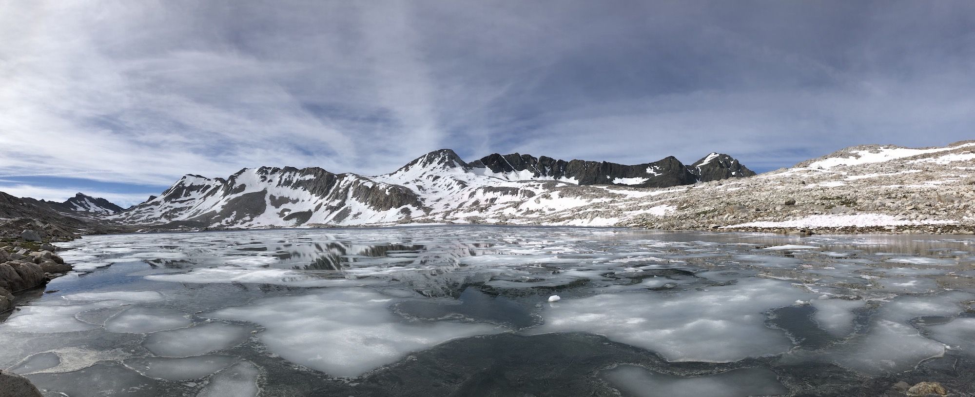 A partially frozen lake with snowy mountains in the background