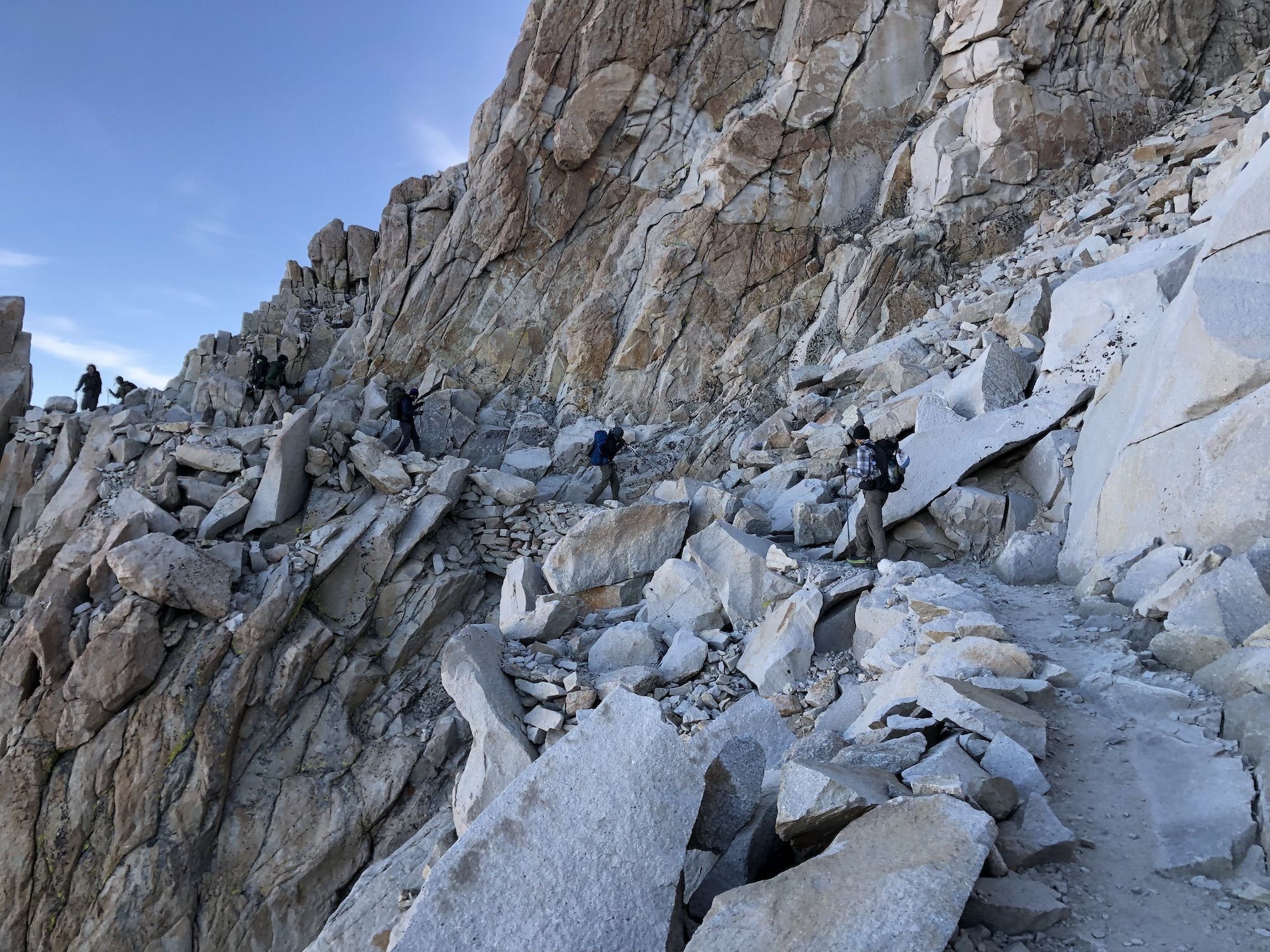 Several hikers on a narrow path cutting through a mountain side.