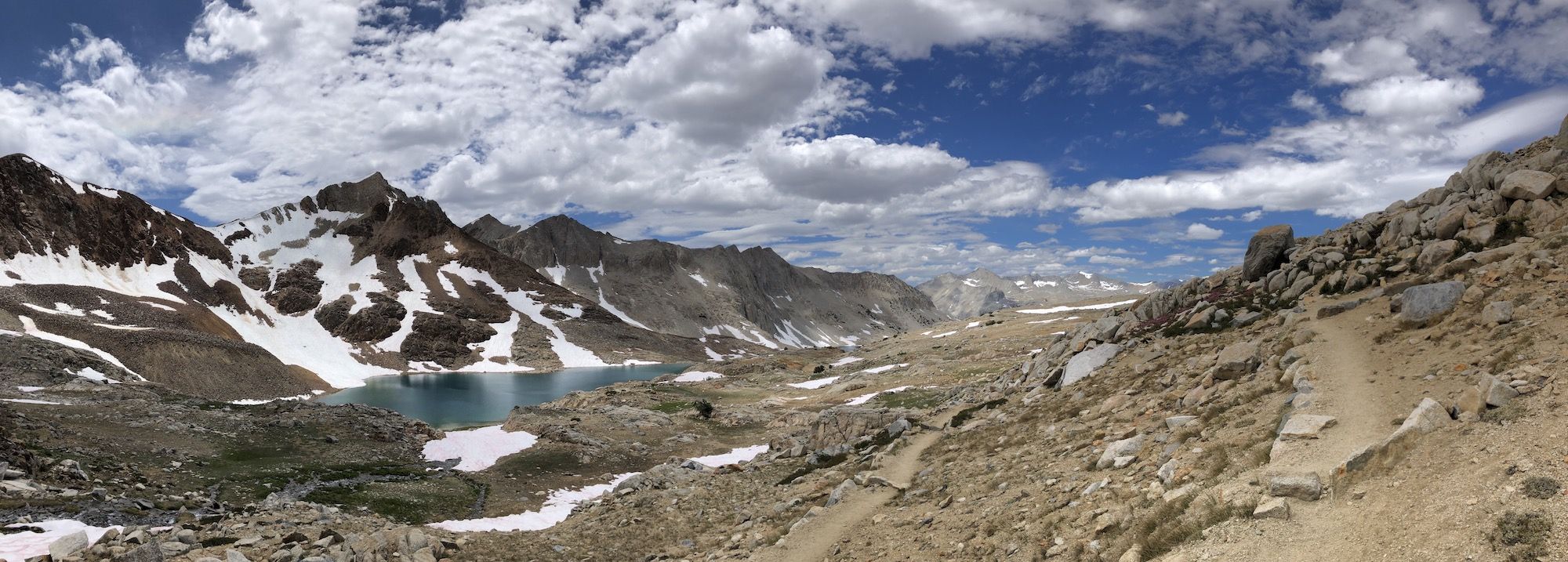 A switchback trail going though a desert-like rocky landscape. A lake can be seen in the distance. 