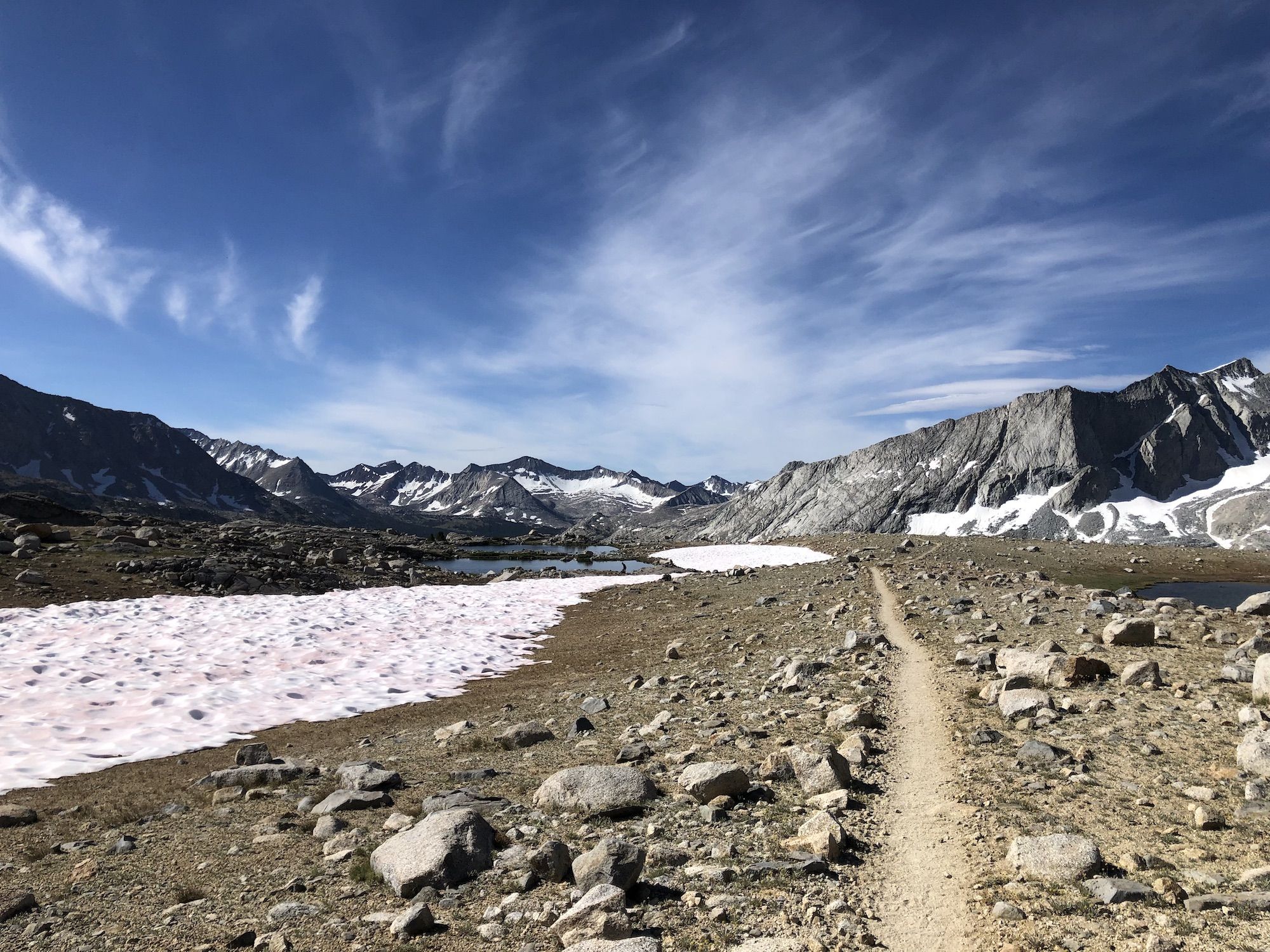 A dirt path going through a rocky landscape with small snow patches.