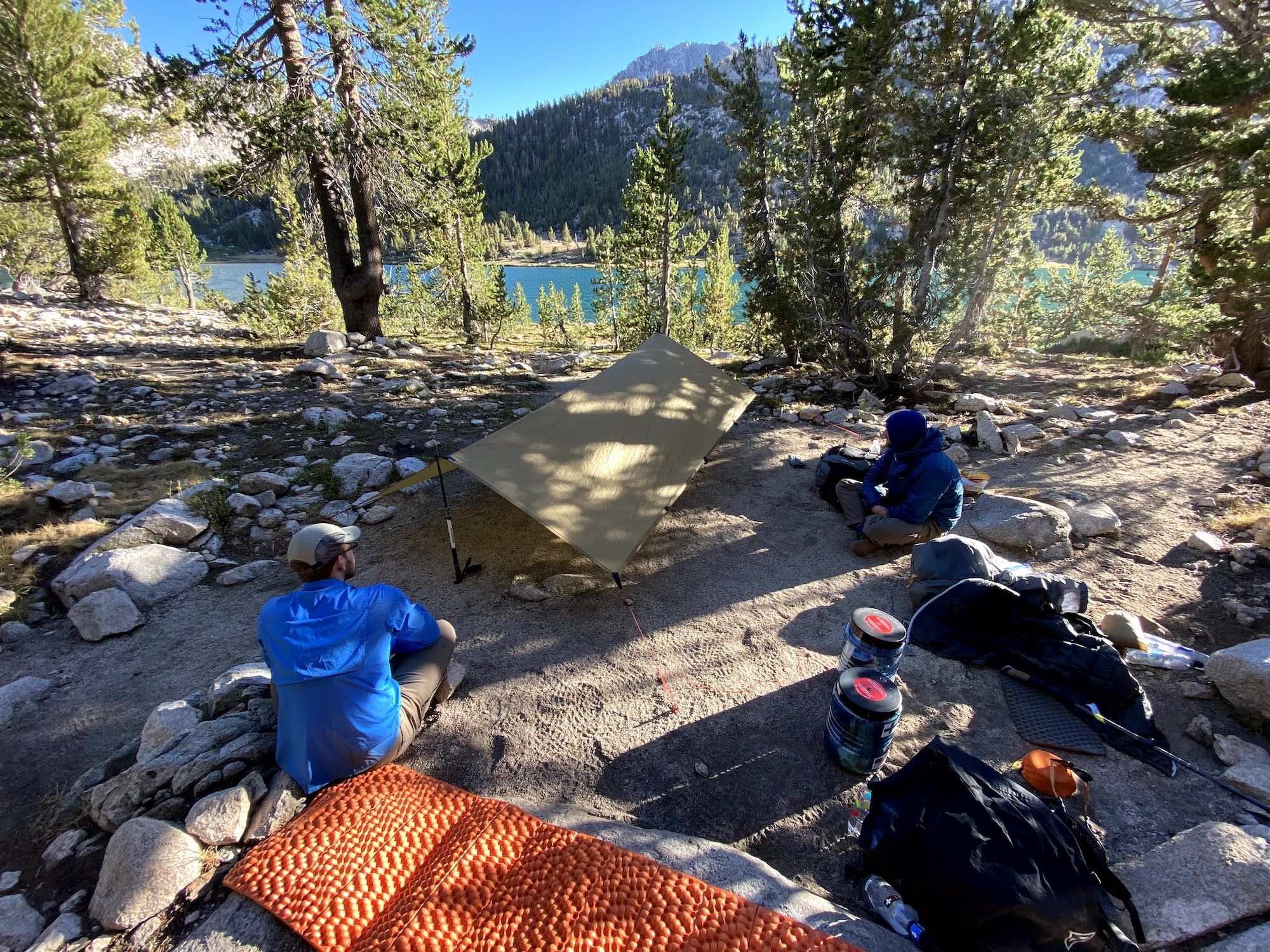 Two men sitting in camp around a tarp