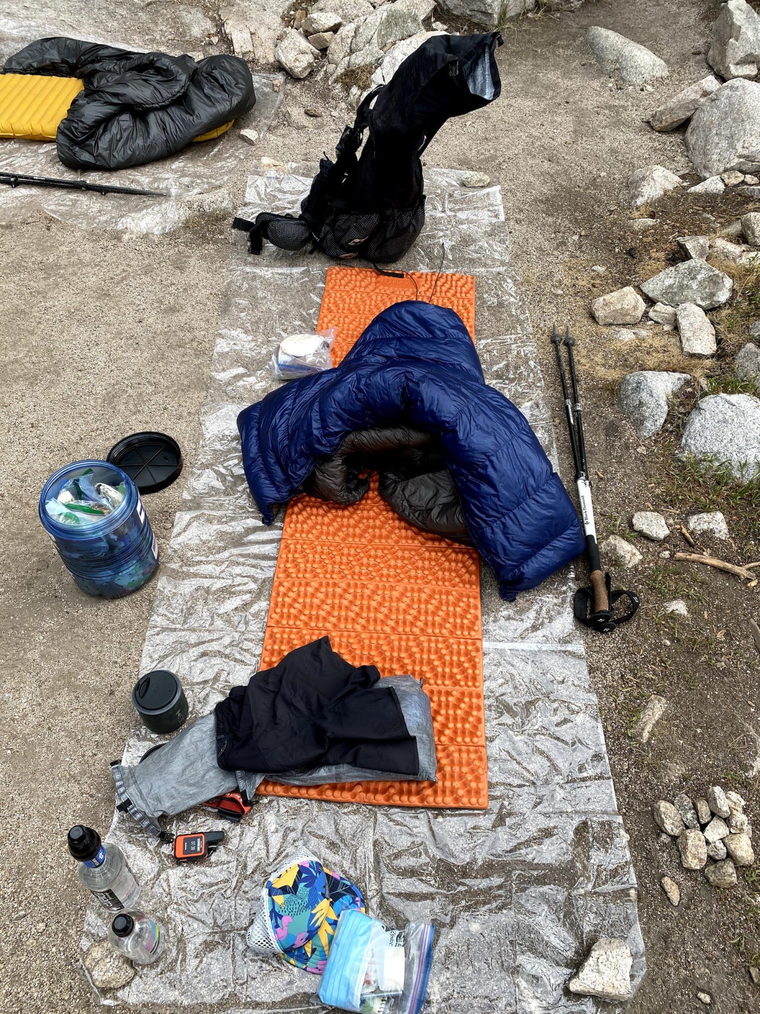 A ground sheet with a sleeping pad and quilt. There is a small pile of rocks next to the sleep setup.