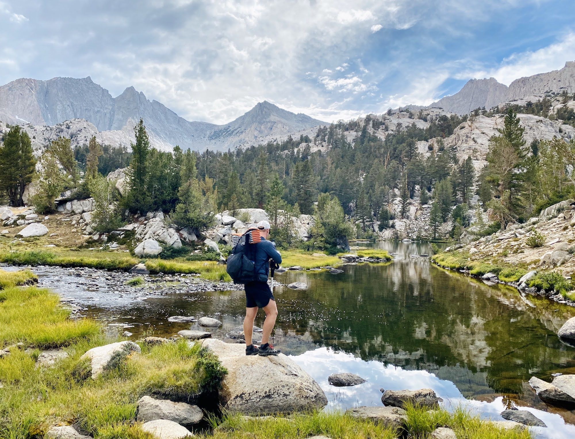 A man standing on a rock overlooking a small creek.