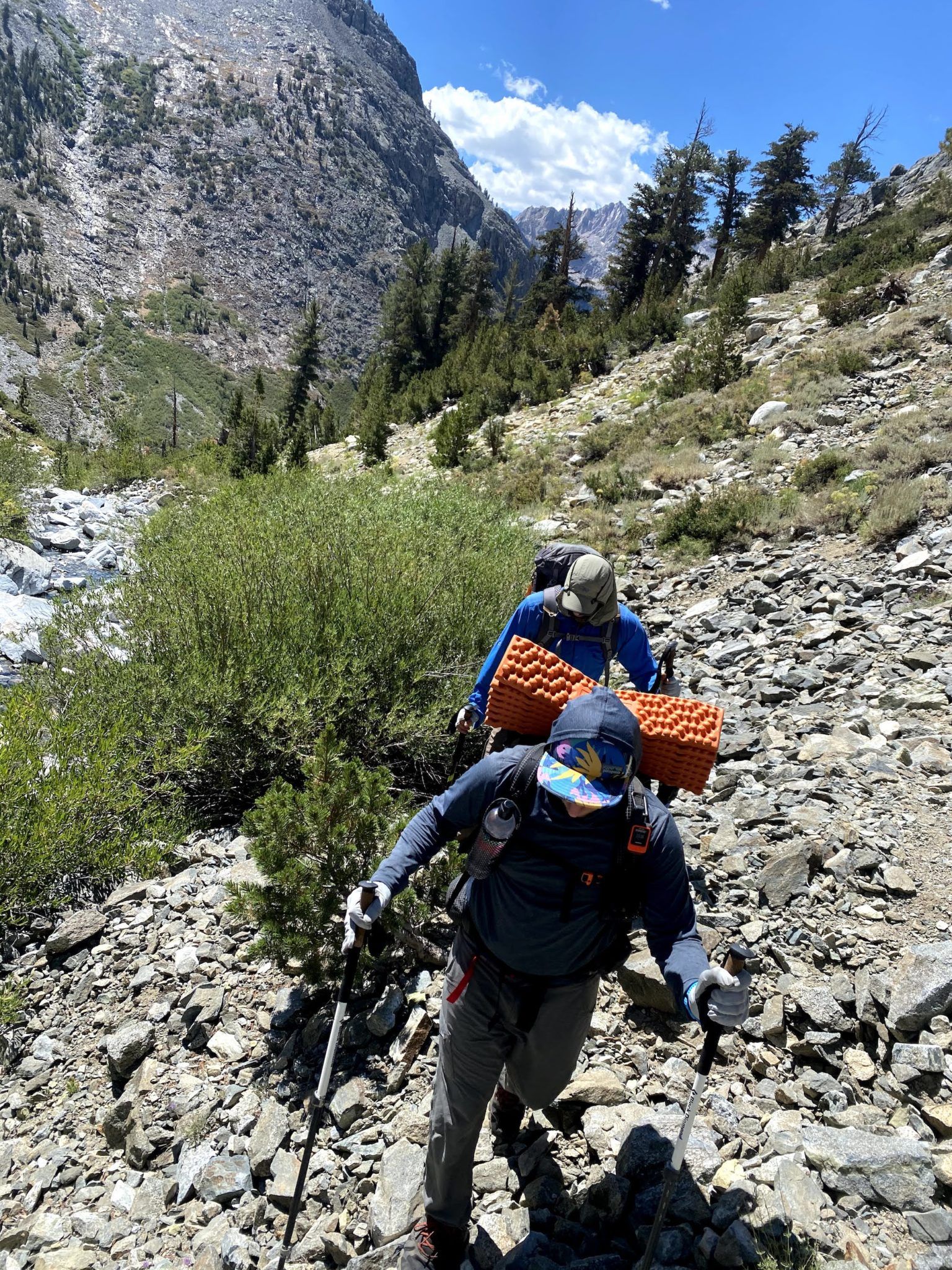 Two men walking on loose rock along a creek.