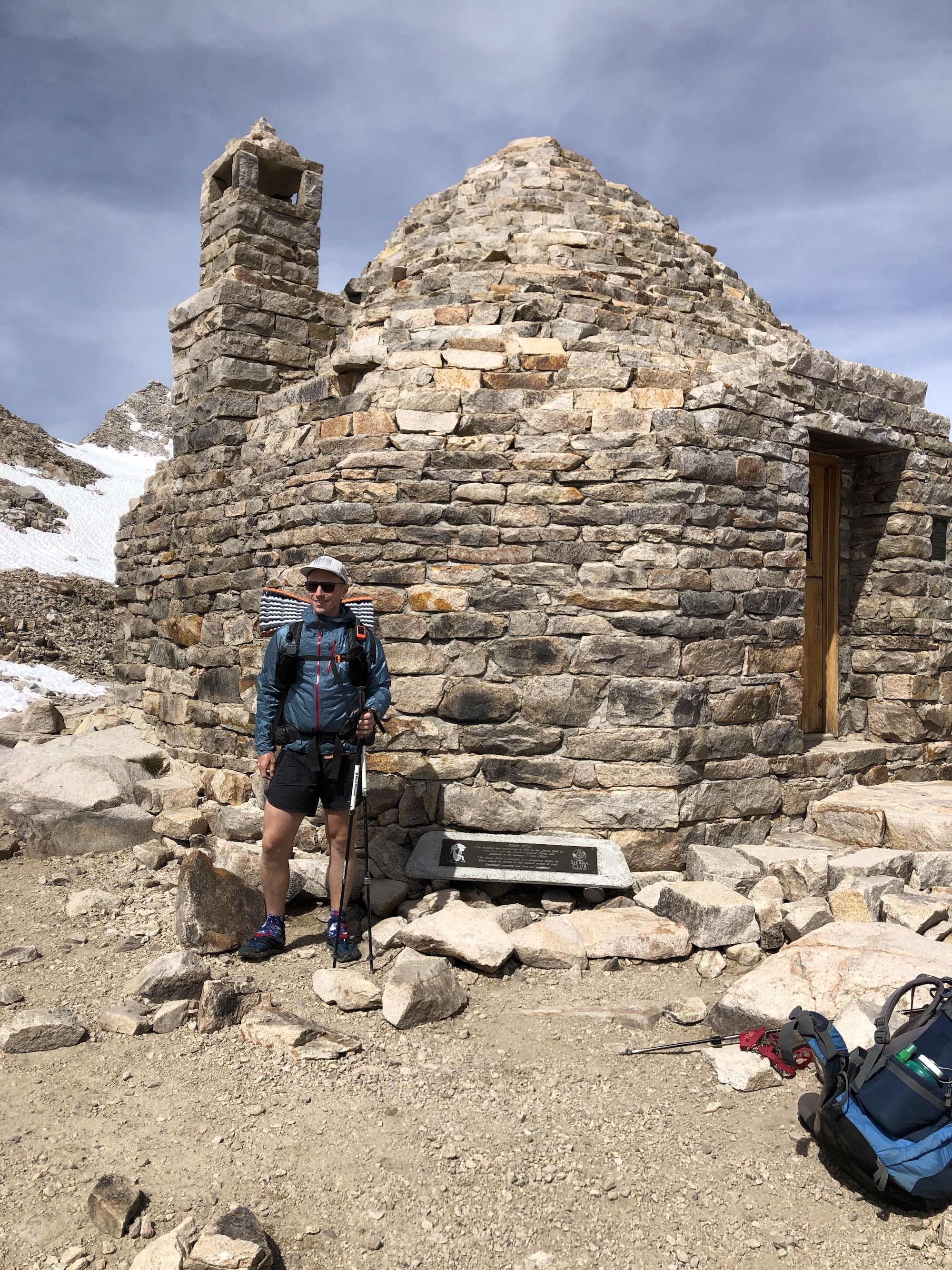 A backpacker standing in front of a stone hut