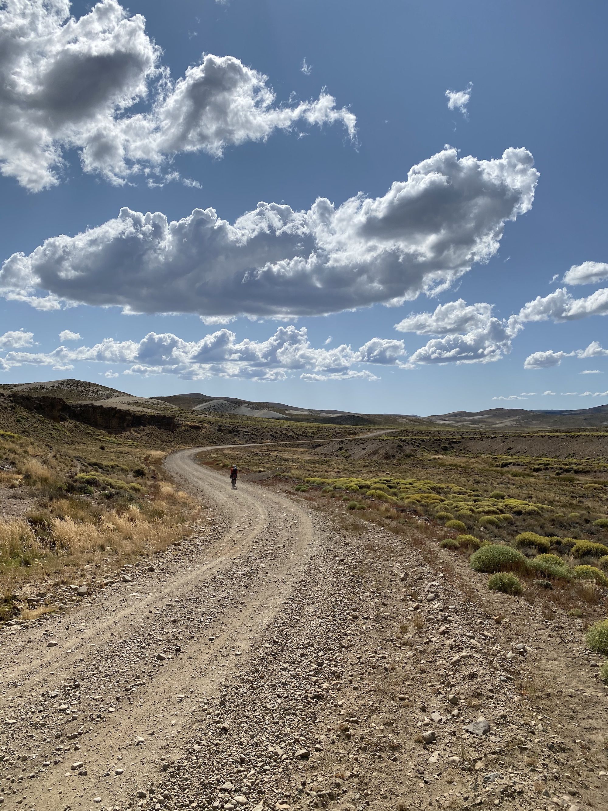 Man riding bike on a long and winding gravel road through a mountain landscape