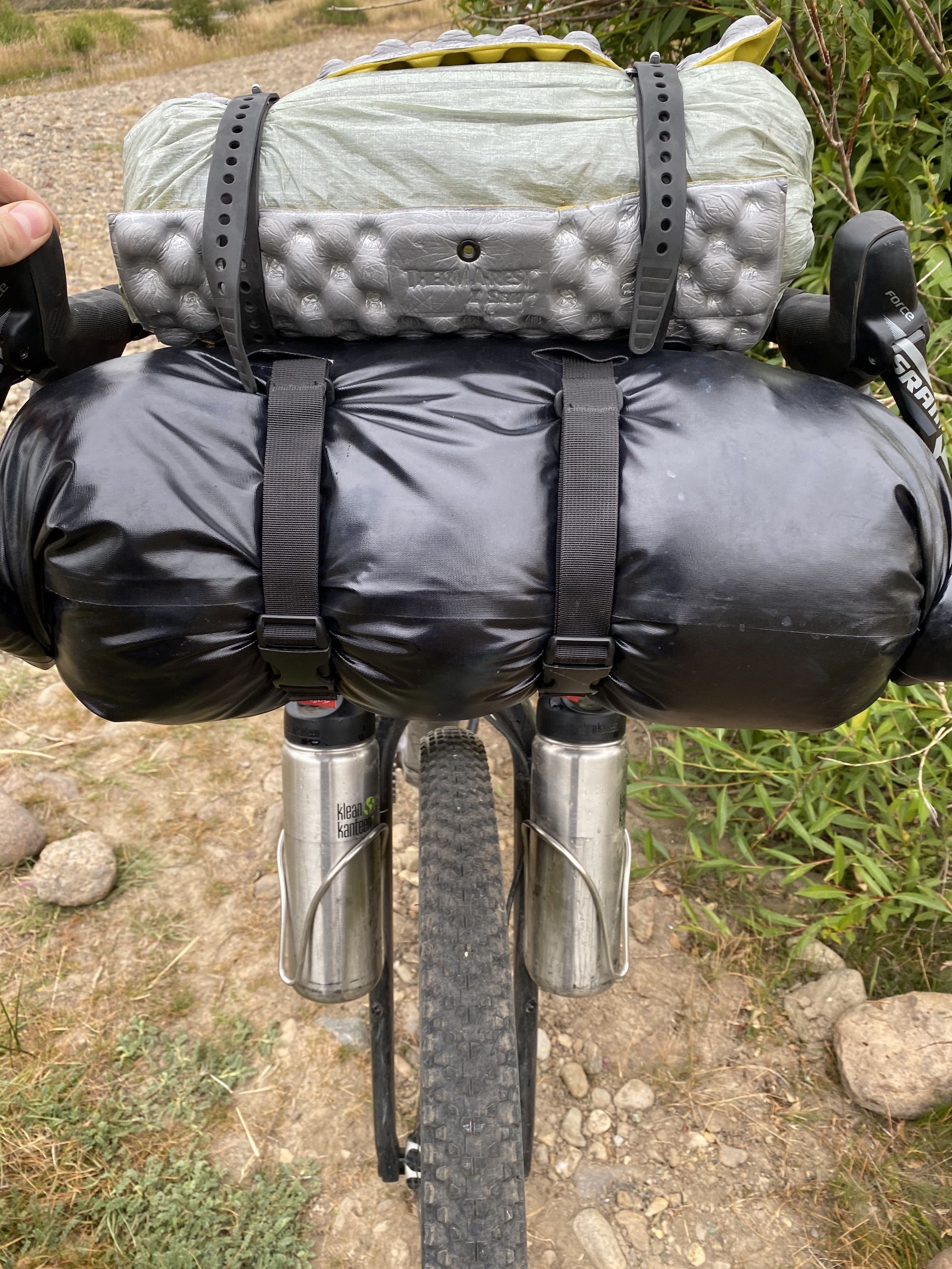Bikepacking bag setup: a foam sit pad around a tent that is strapped to the handlebars of a bike