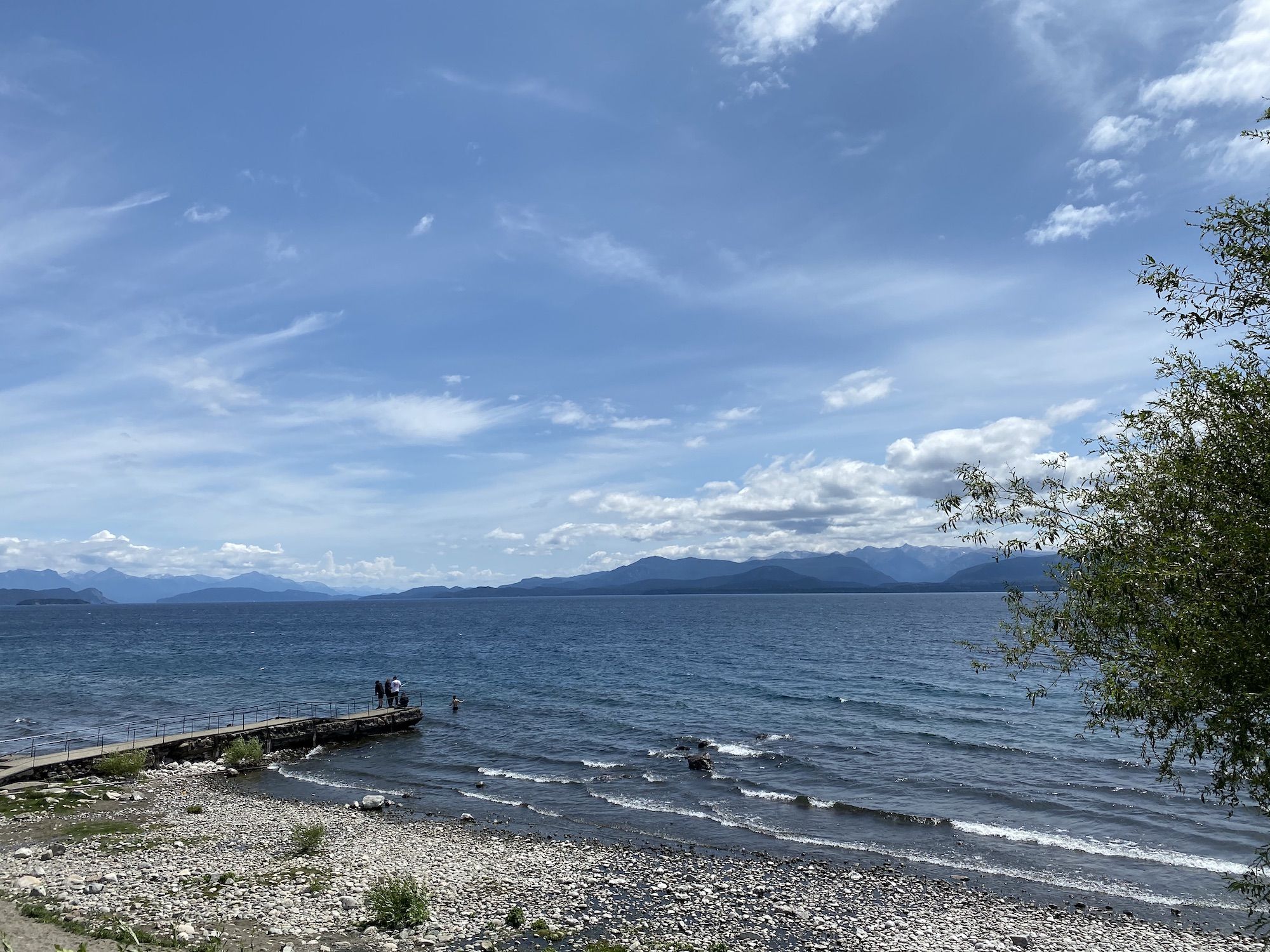 A lakeshore with a pier and mountains in the background