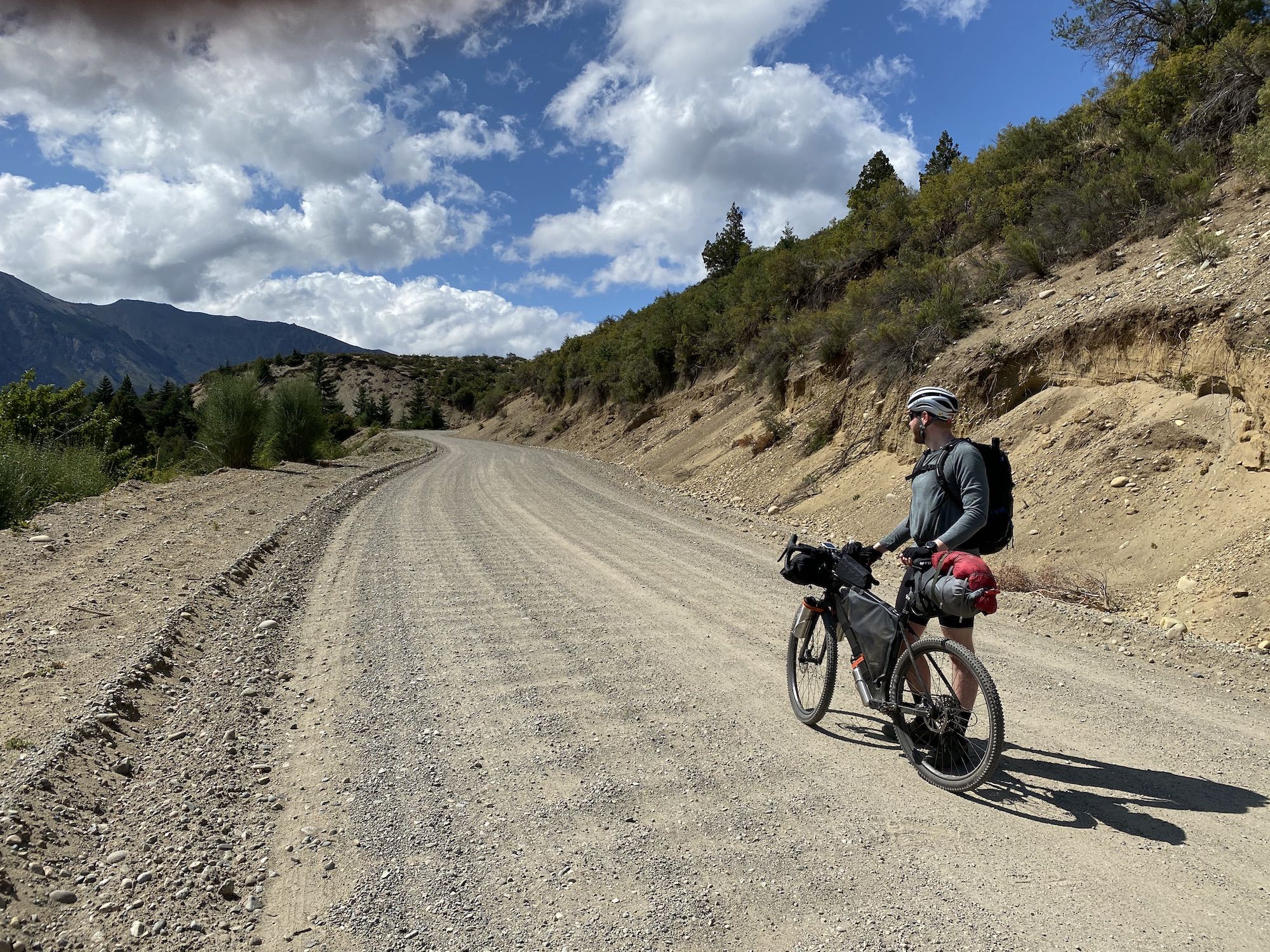 A man standing with his bike on a gravel road.