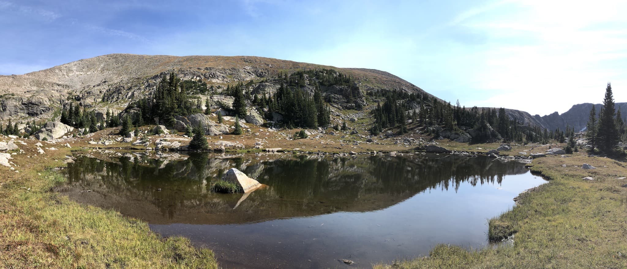 A panoramic view of a small pond with mountains in the background.