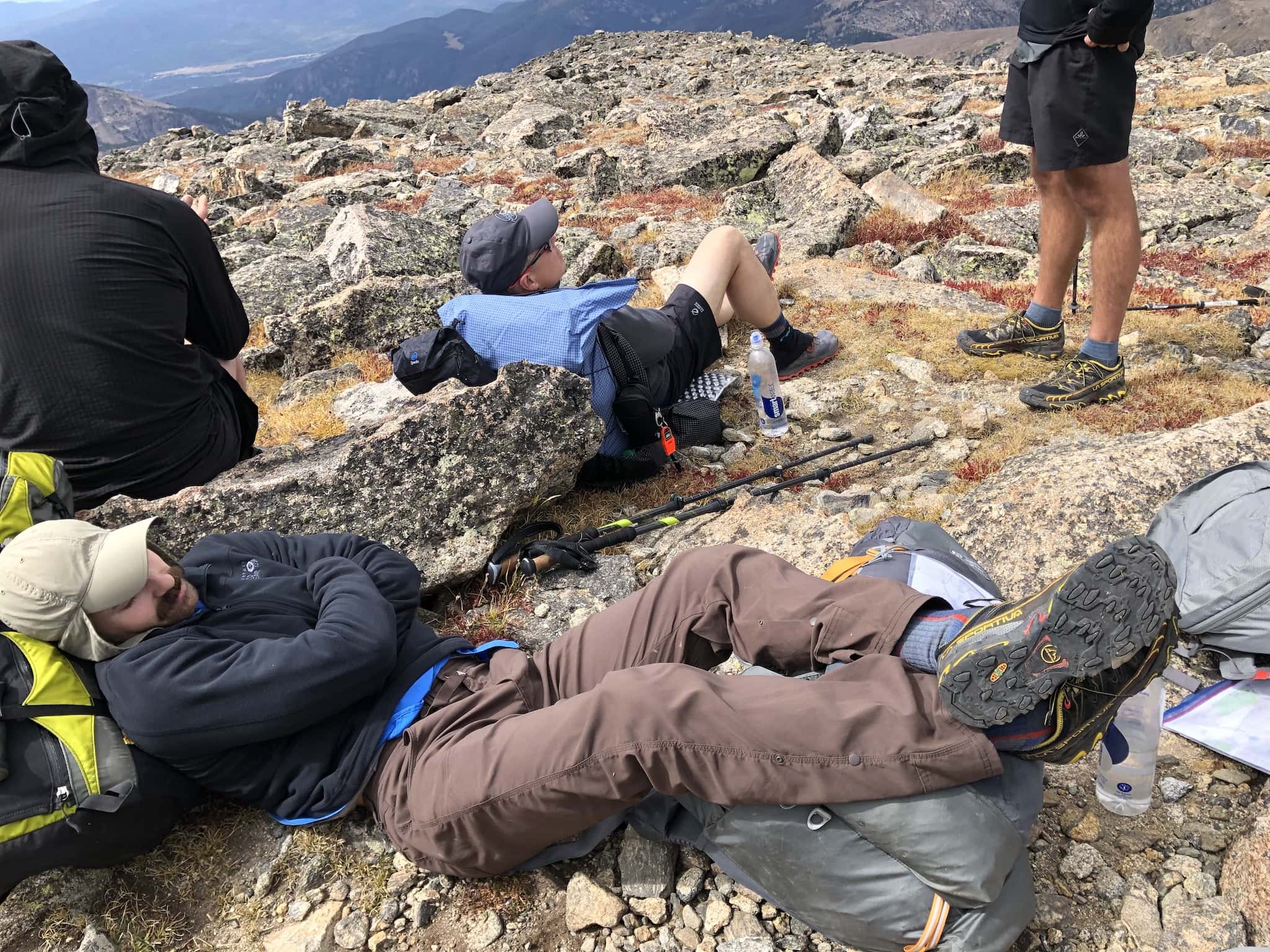 A man sleeping, leaning his head against a backpack and his feet on another backpack.