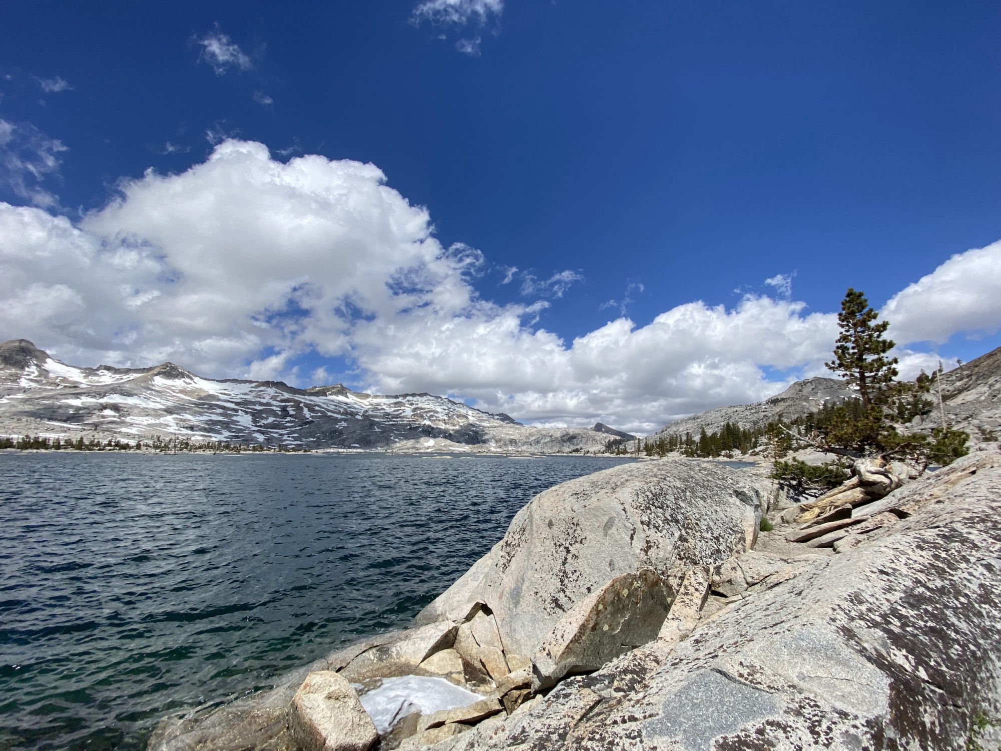 A lake with a snowy mountain range on the far side and white granite cliffs on the near shore.