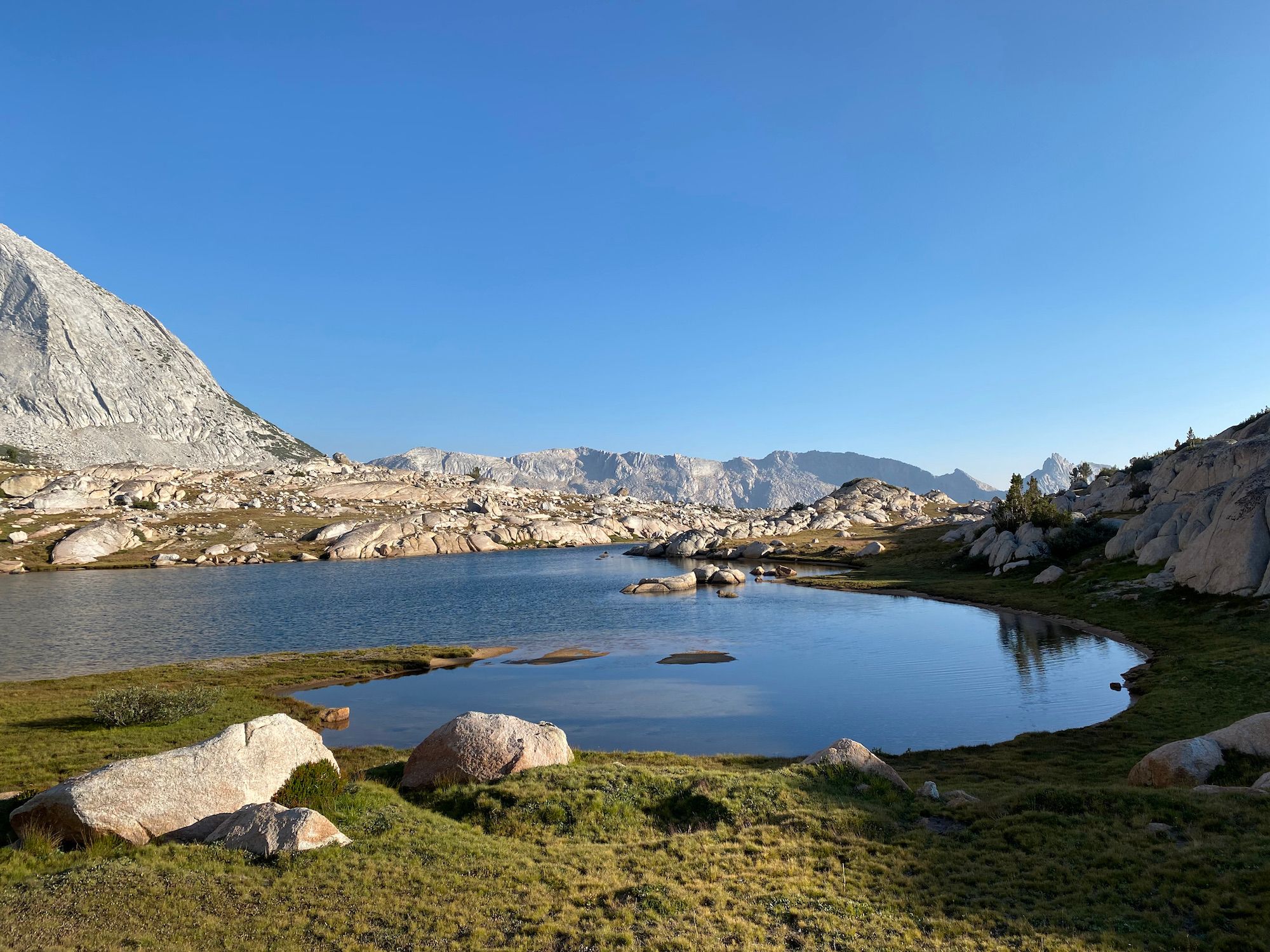 A calm lake surrounded by grassy meadows and rounded boulders.
