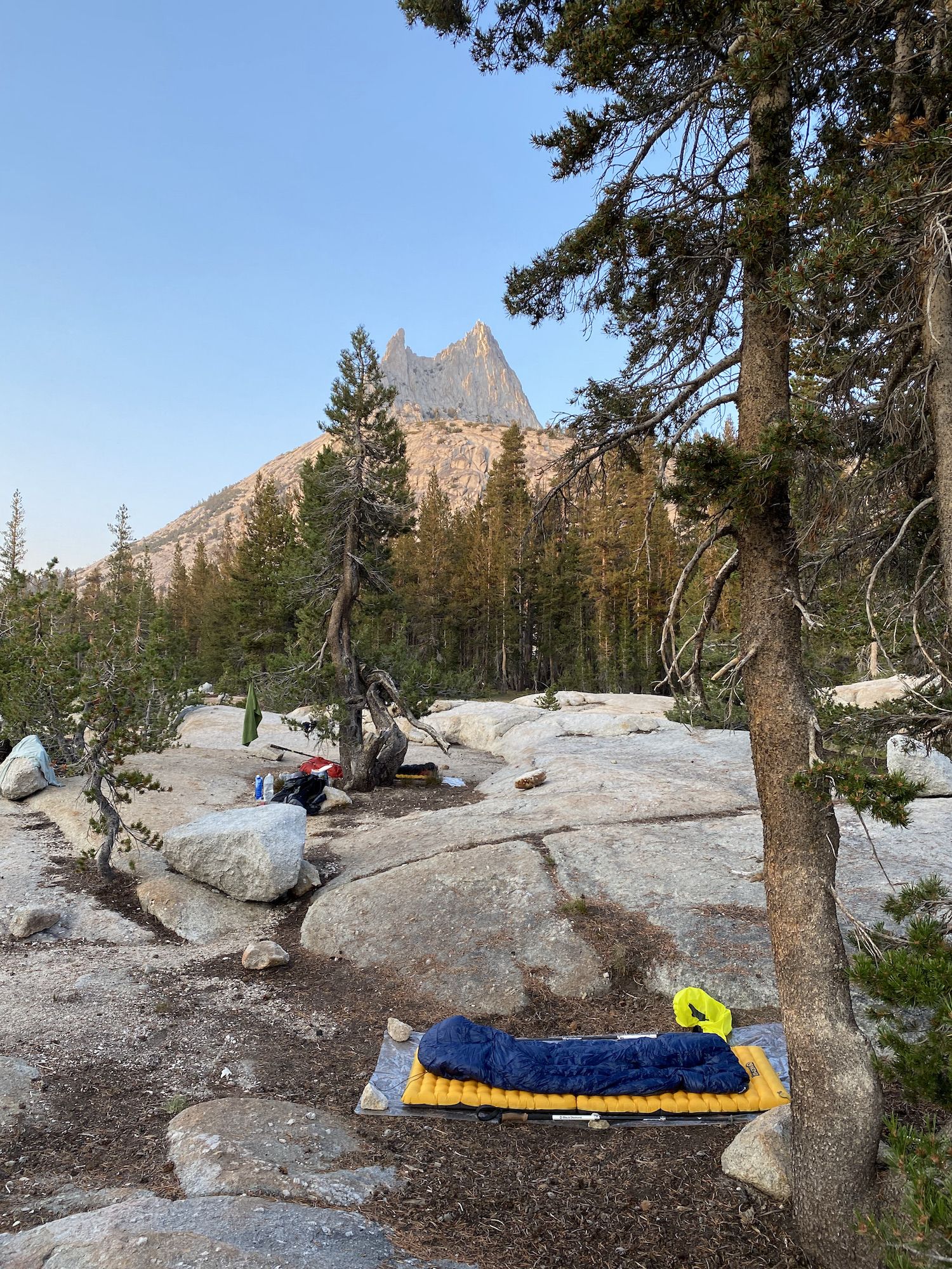 Two cowboy camp setups nestled between granite slabs. A jagged mountain peak in the distance behind the camp.