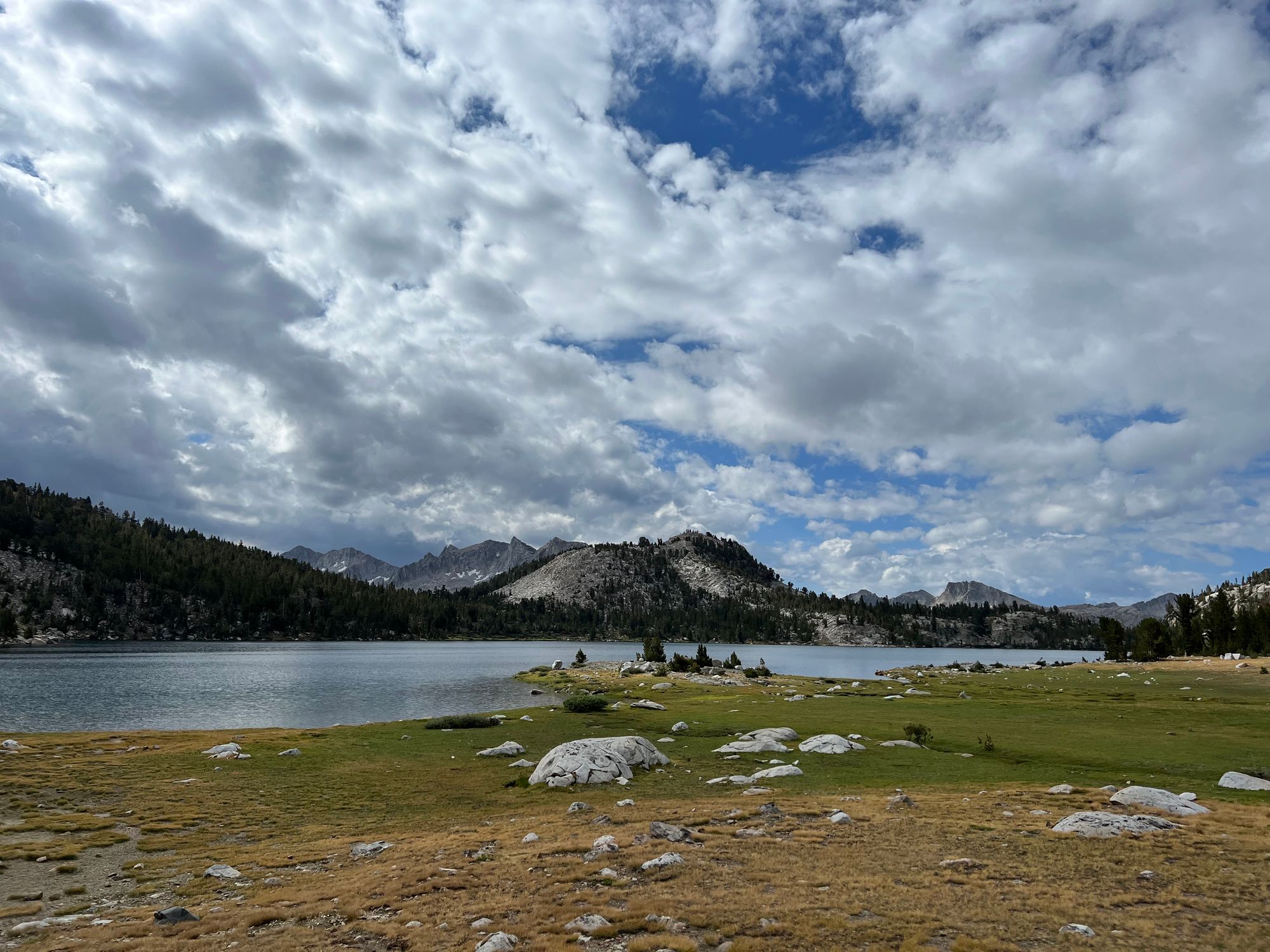 A lake with a meadow in the foreground. Dark clouds are moving in from the left. 