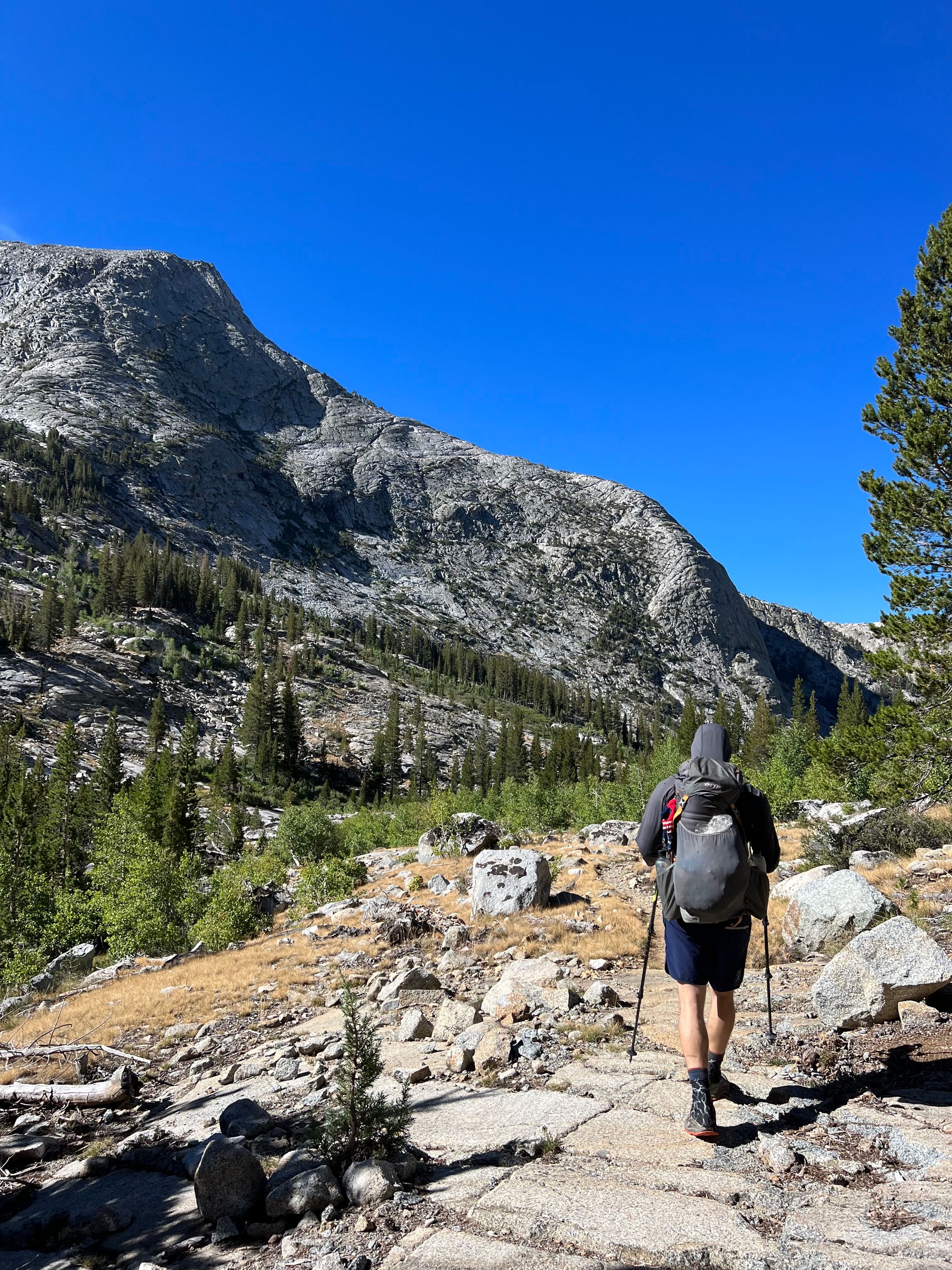 A backpacker walking along a trail through a mountain valley.