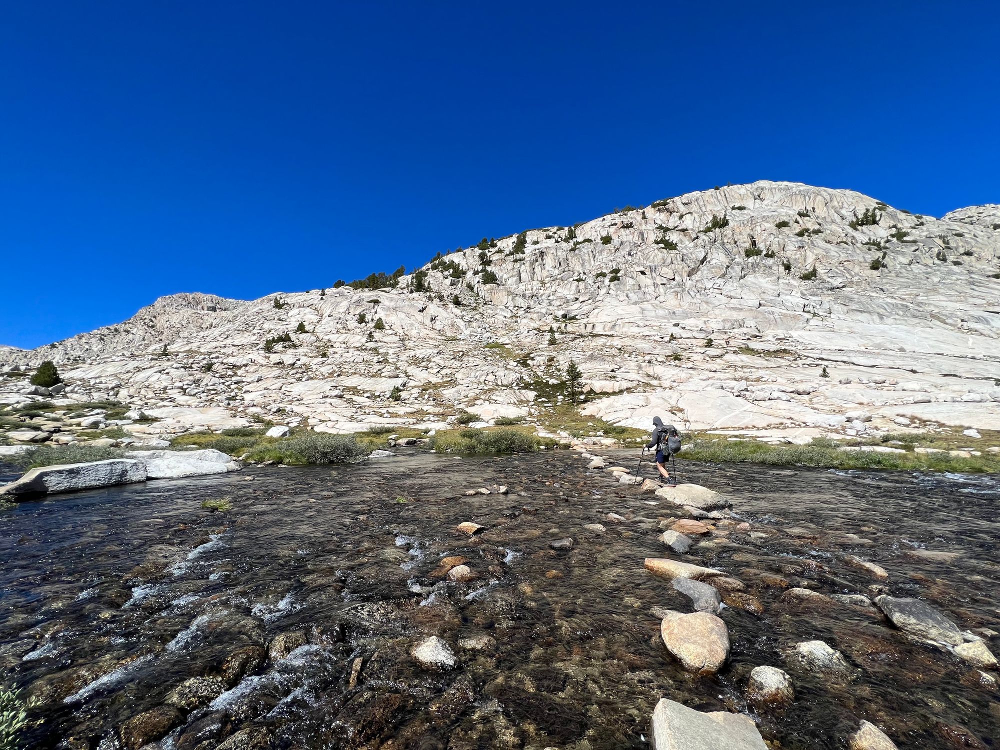 A backpacker walking along rocks over a wide creek.