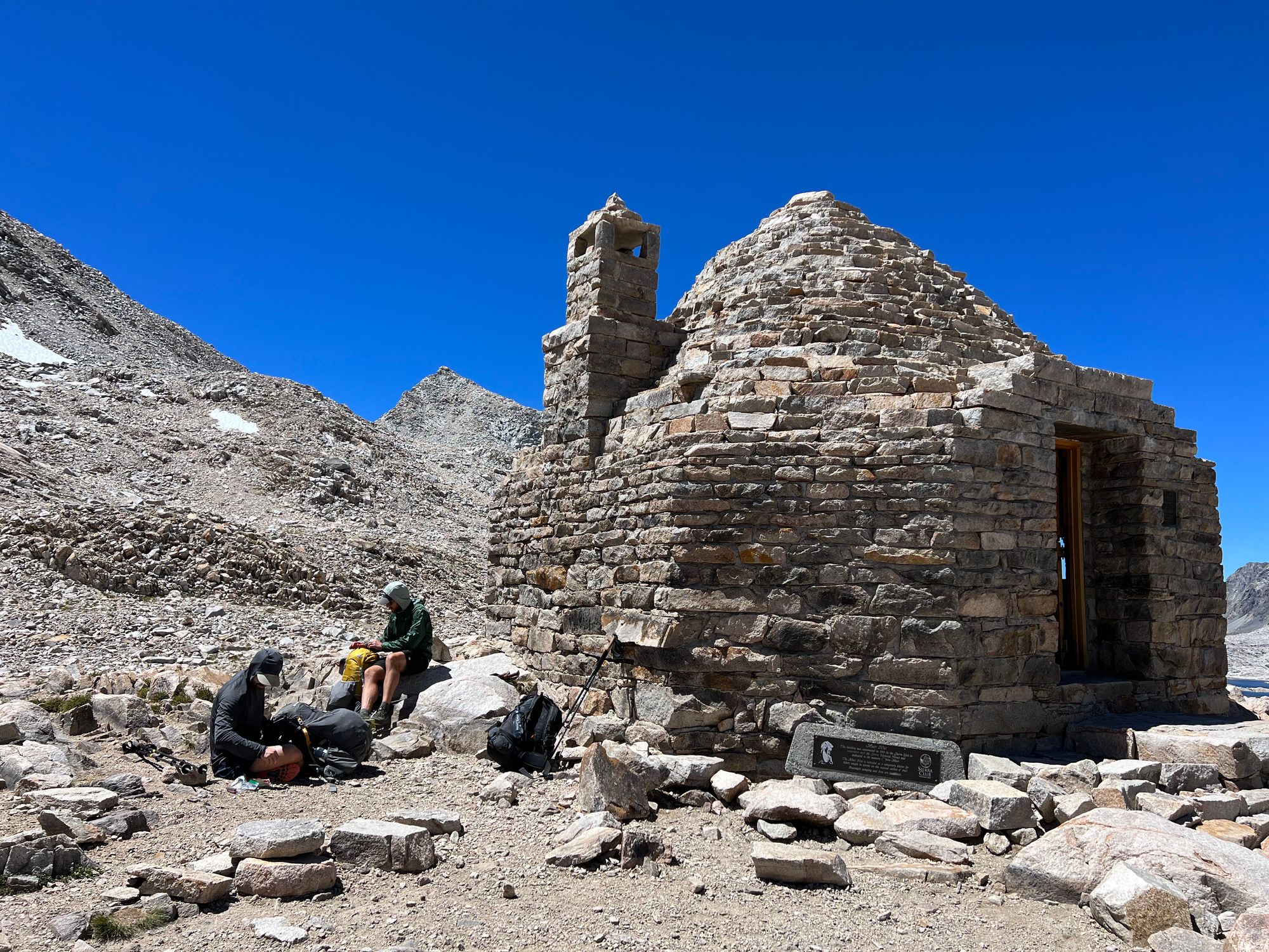 Two backpackers sitting outside a stone hut.