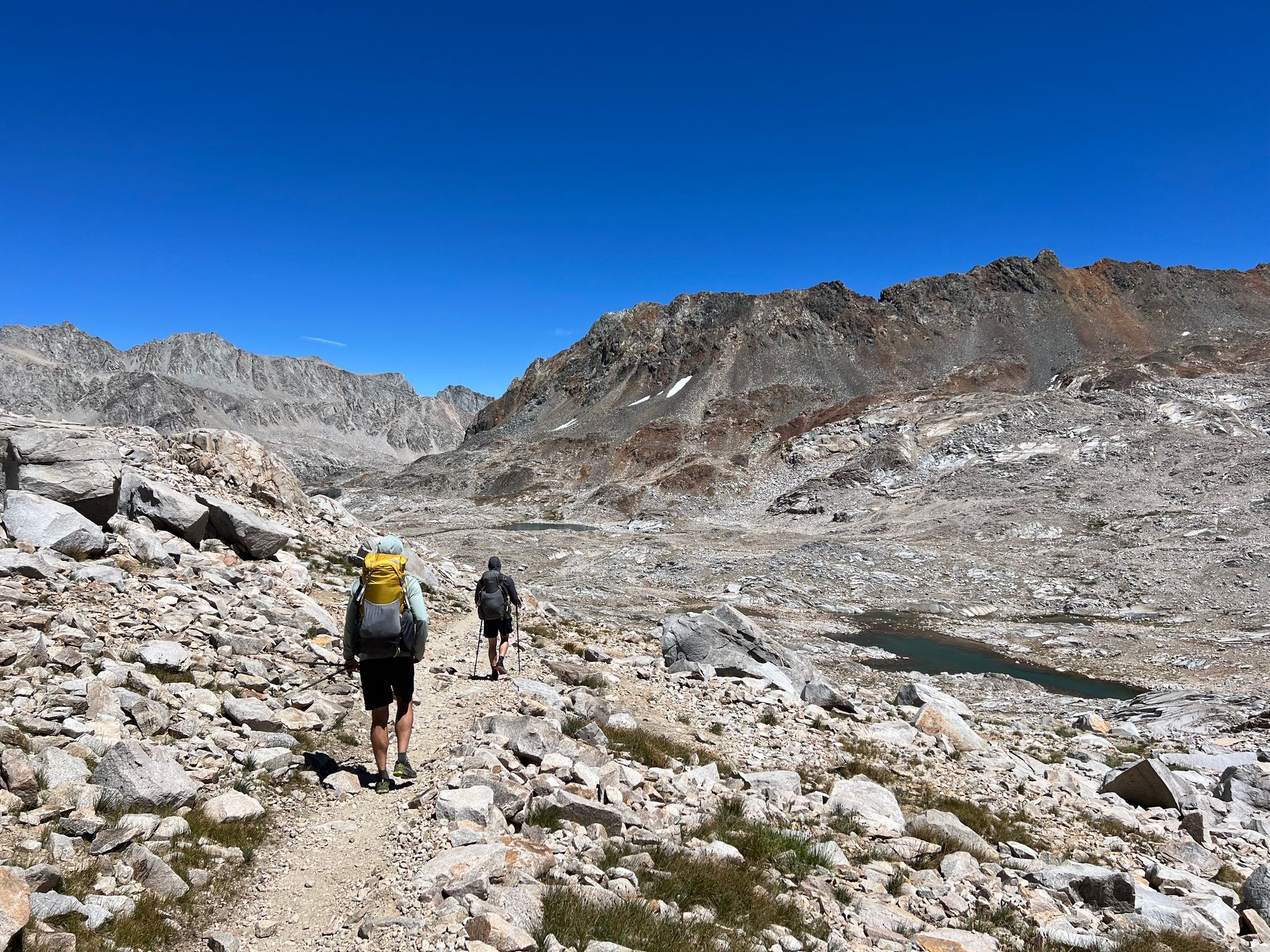 Two backpackers walking through rocky terrain.